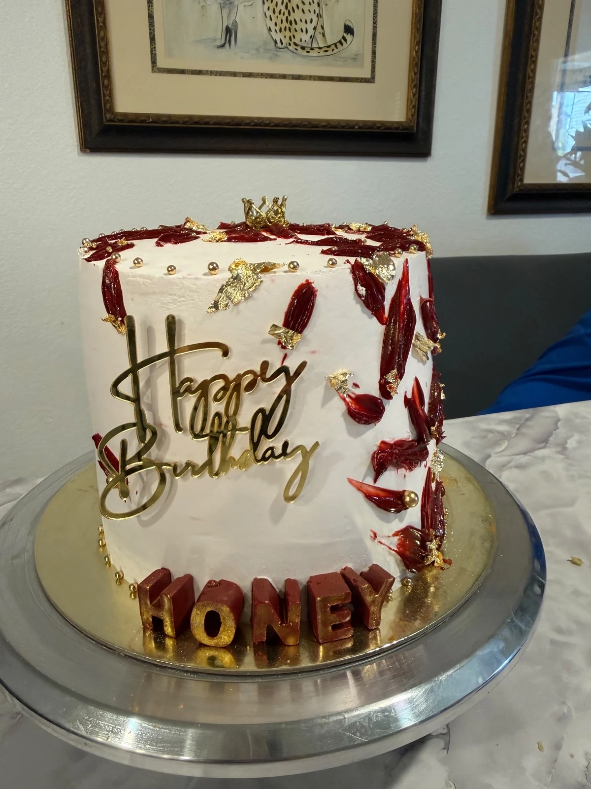 White cake with red and gold decorations, a crown, and a Happy Birthday topper