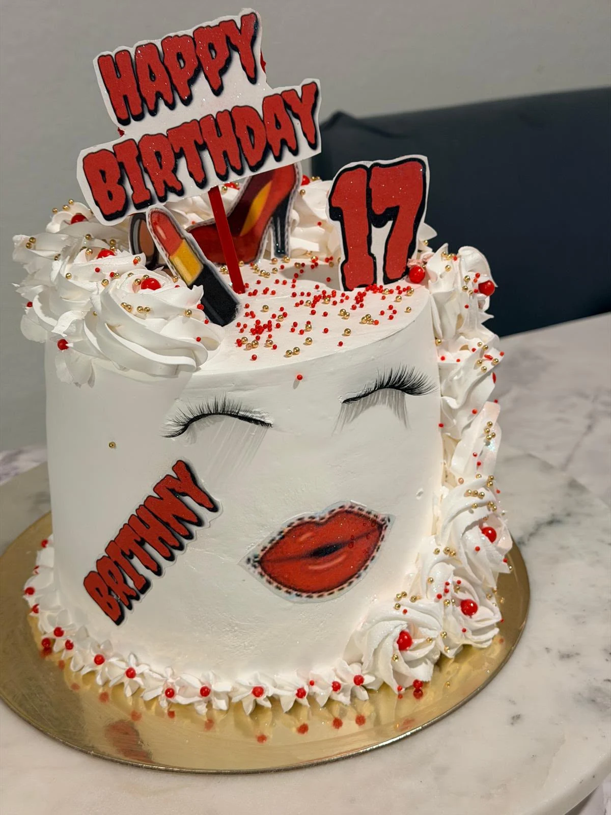 White birthday cake with red decorations, eyelashes, lips, and a number 17 topper